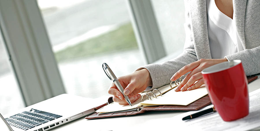 Businesswoman sitting at desk and makes a note in office.